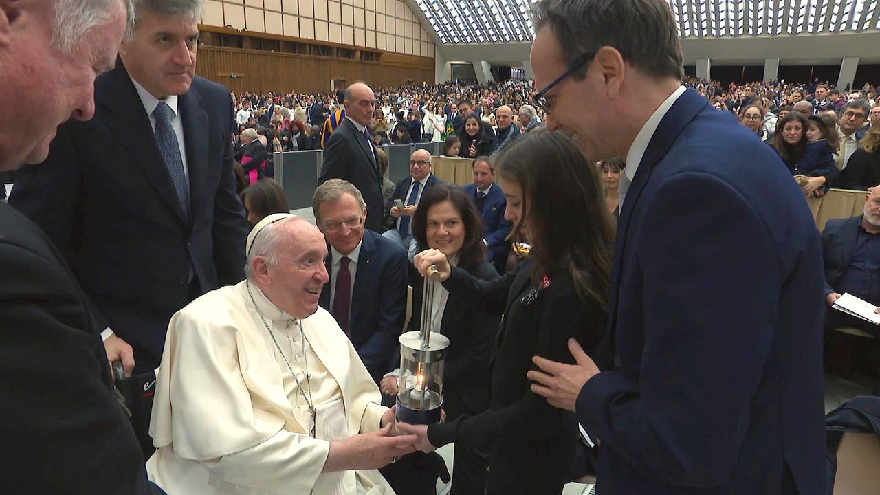 Papst Franziskus wird vom Friedenlicht-Kind Sarah das ORF Friedenslicht übergeben. Rundherum sehen sehr viele Menschen zu.